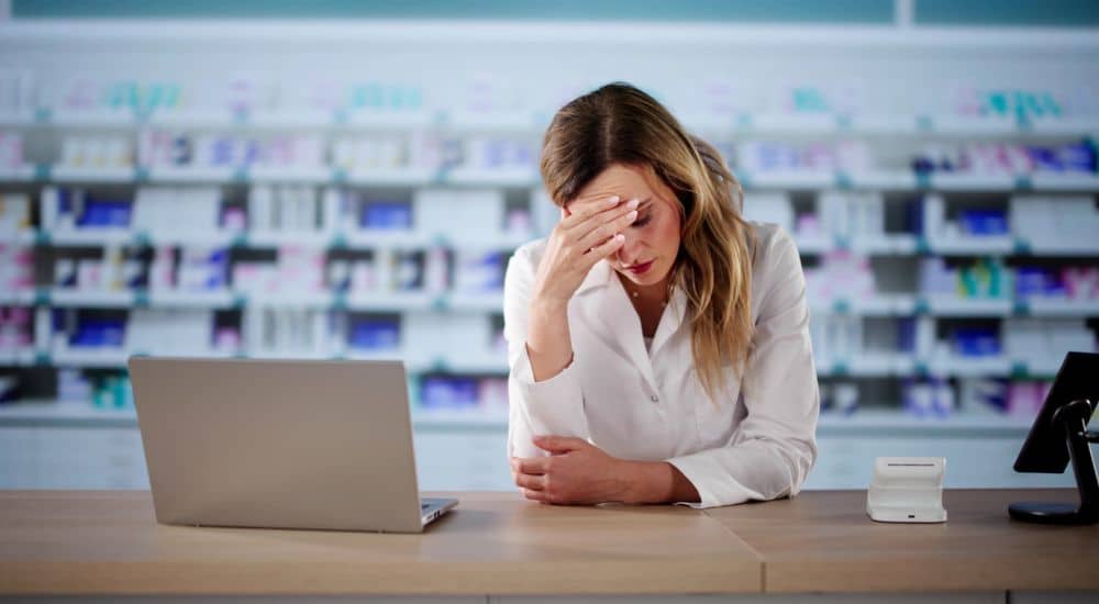 Pharmacienne à son comptoir se tenant le front. Biosimilaires
