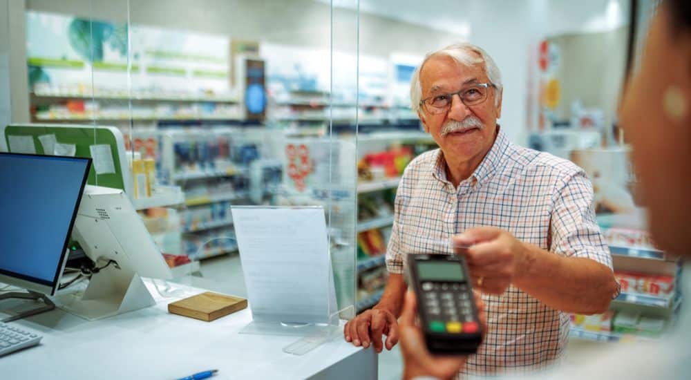 Patient âgé réglant ses médicaments en carte bancaire à la pharmacie, fin annoncée du remboursement intégral des SMR faibles